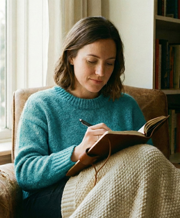 A woman writes in her journal while sitting in a comfortable chair.